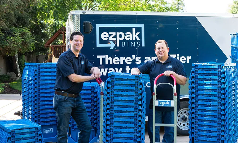 EZPak movers standing next to dolly carts and plastic bins ready to make your next move more convenient