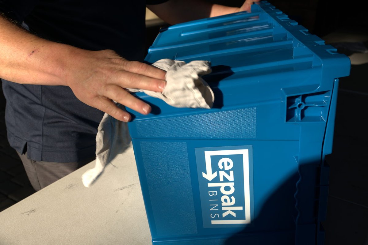 A close-up of a hand using a cloth to wipe down a clean blue EZPak Bins branded moving crate