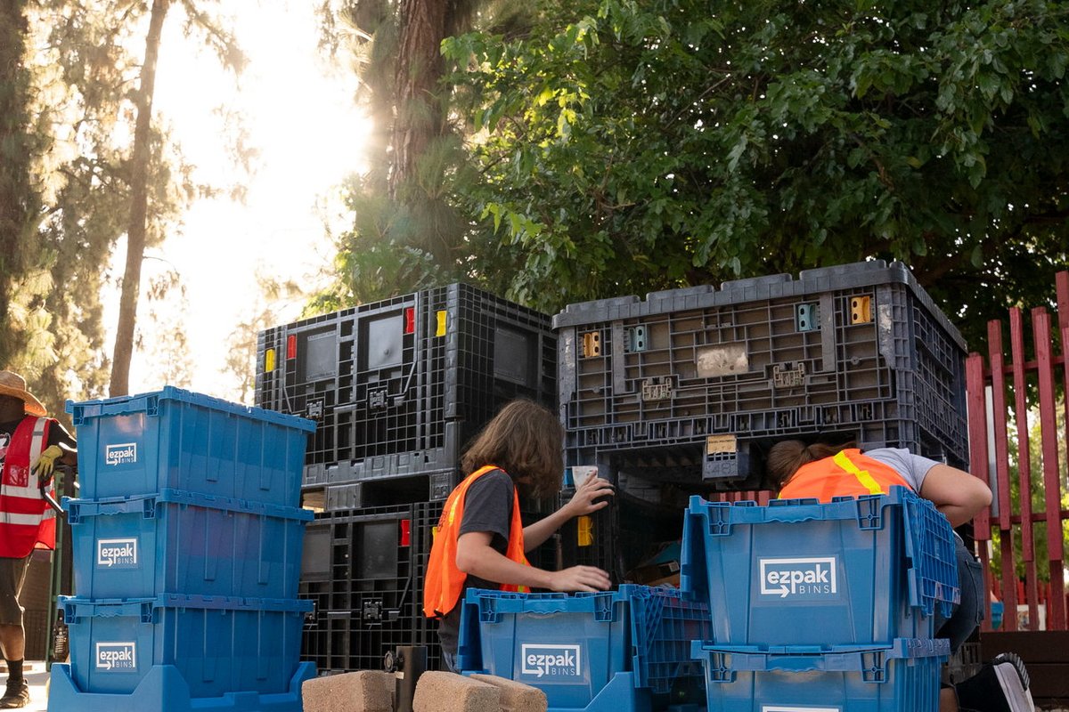 A crew sorts supplies into blue EZPak Bins moving crates near large storage containers outdoors