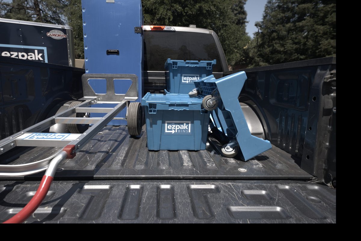 Blue EZPak Bins moving bins and a hand truck loaded in a pickup truck bed, with a branded EZPak box truck parked behind