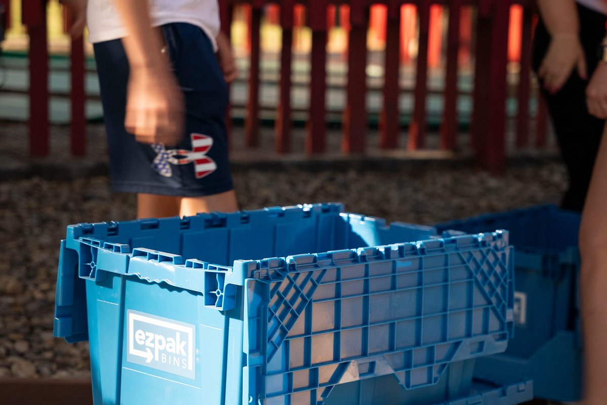 Open blue EZPak Bins moving crates sit outdoors by a red fence as people pass by
