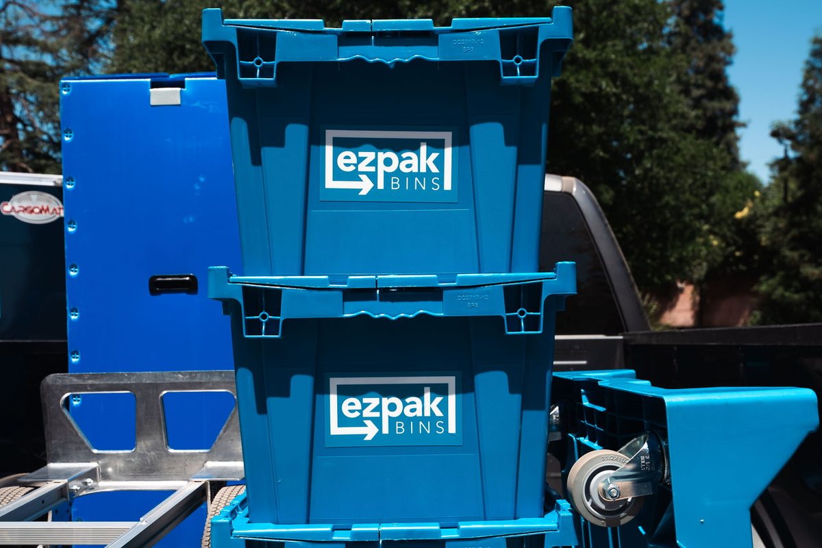 Three blue EZPak Bins moving bins stacked in the bed of a pickup truck next to a hand dolly, parked outdoors