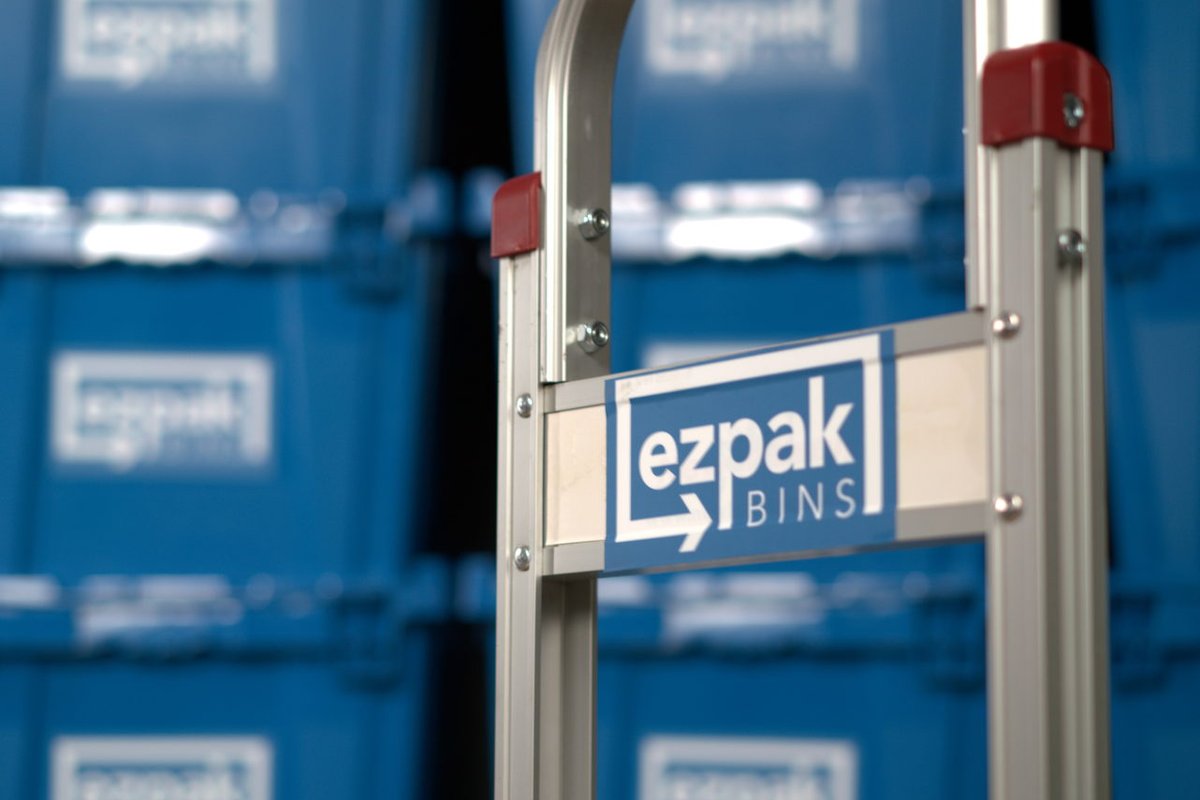 A close-up of an EZPak Bins branded hand truck with a red handle in front of rows of stacked blue moving bins