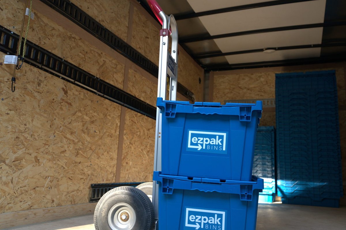 An EZPak Bins branded hand truck loaded with two stacked blue moving bins standing upright inside a cargo trailer