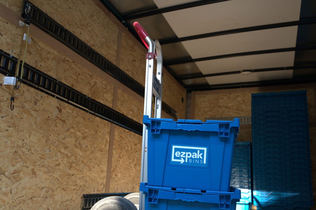 A blue EZPak Bins moving crate on a hand truck inside a cargo trailer