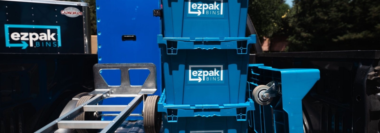 Three blue stackable EZPak Bins moving crates and a hand dolly loaded on a branded delivery trailer, ready for rental drop-off in Fresno