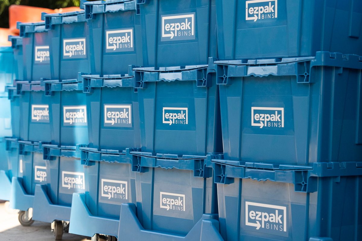 Rows of stacked blue EZPak Bins moving crates on wheeled dollies lined up on a concrete driveway