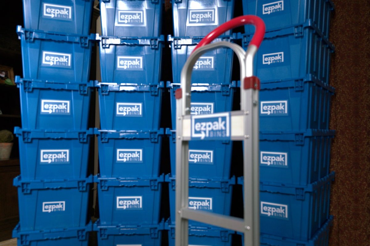 Rows of stacked blue EZPak Bins moving bins with a branded hand truck leaning against them in a home entryway with tile flooring