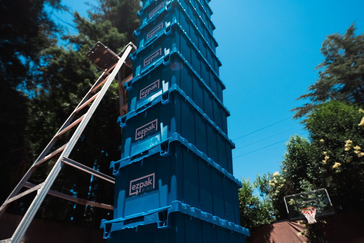 A very tall stack of blue EZPak Bins moving crates against a blue sky on an outdoor court