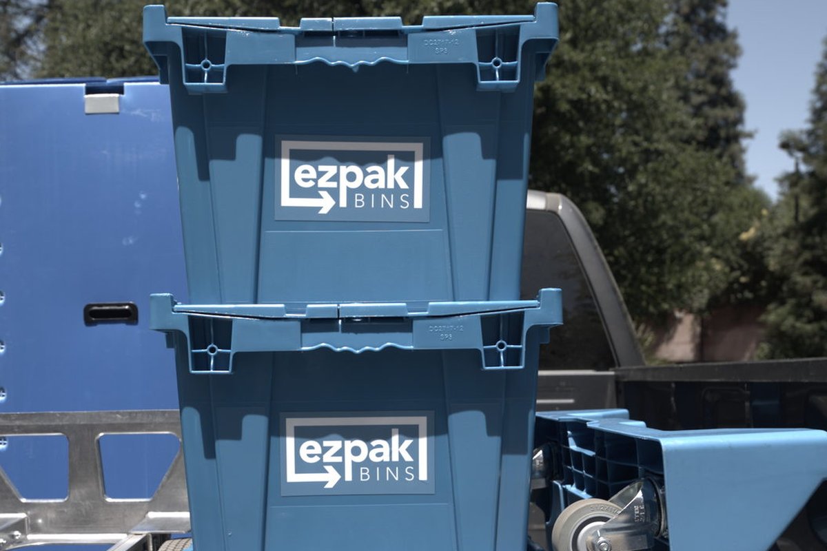 Three blue EZPak Bins moving crates and a hand dolly stacked in the bed of a pickup truck