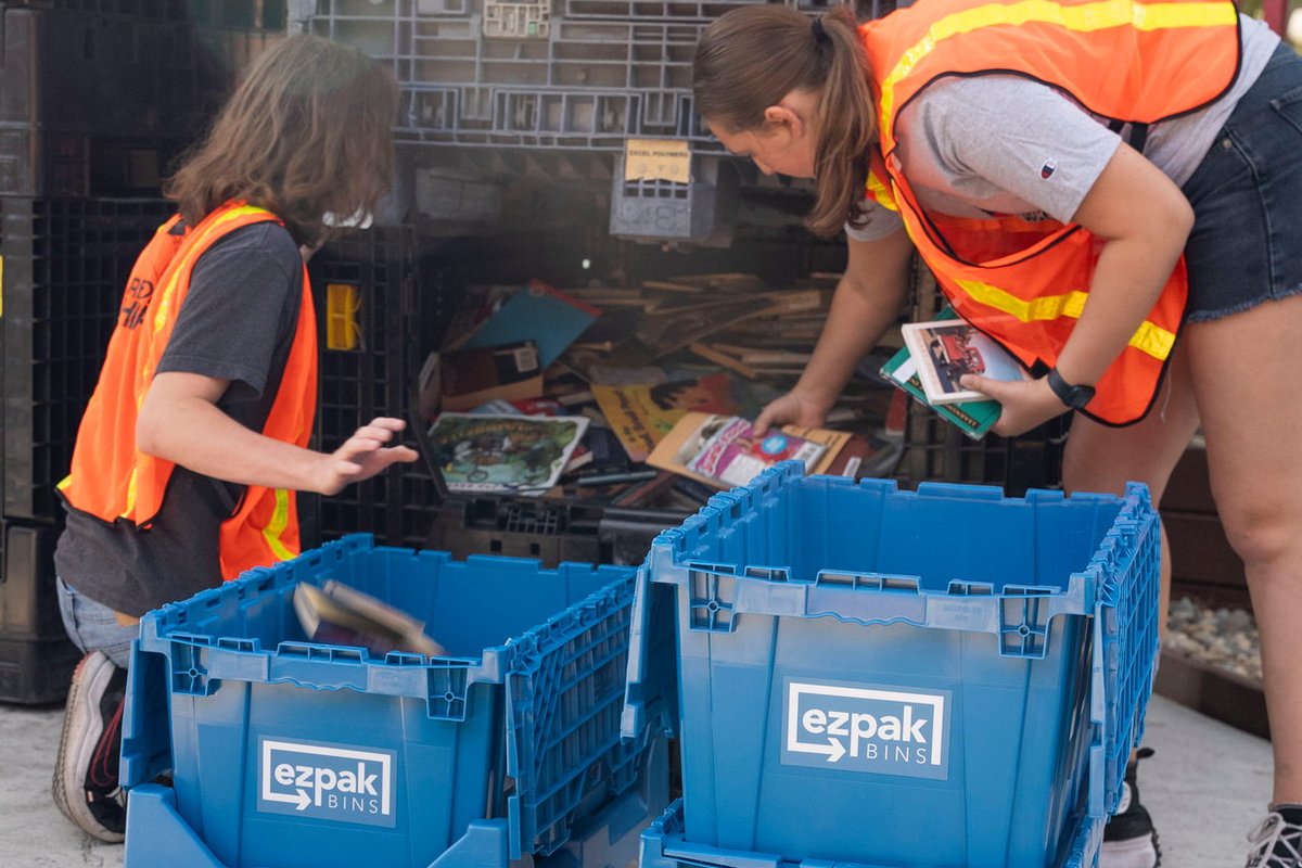 Two people in safety vests sort items into blue EZPak Bins moving crates outdoors